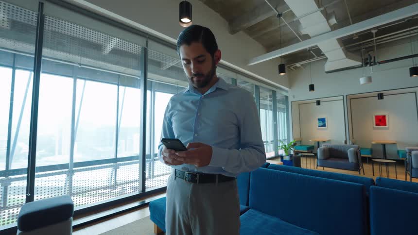 A handsome businessman in a modern office lounge checks his messages on a smartphone