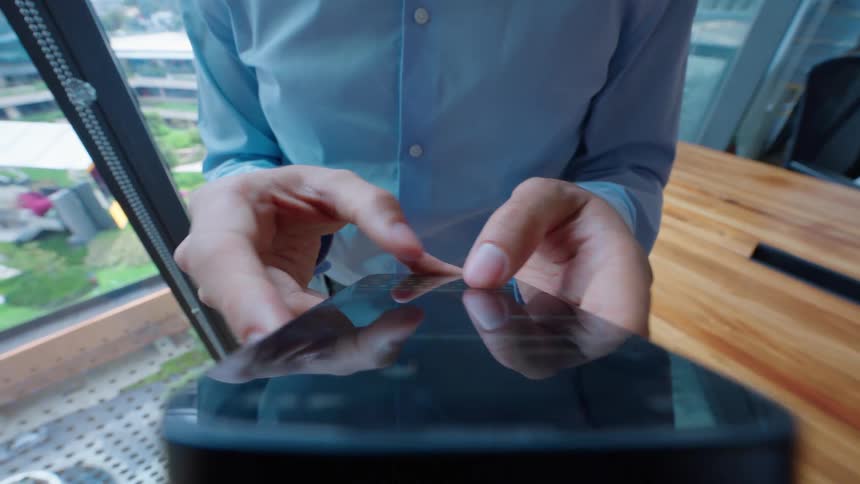 Close-up of a businessman in a blue shirt using his fingers to type and scroll on a modern smartphone