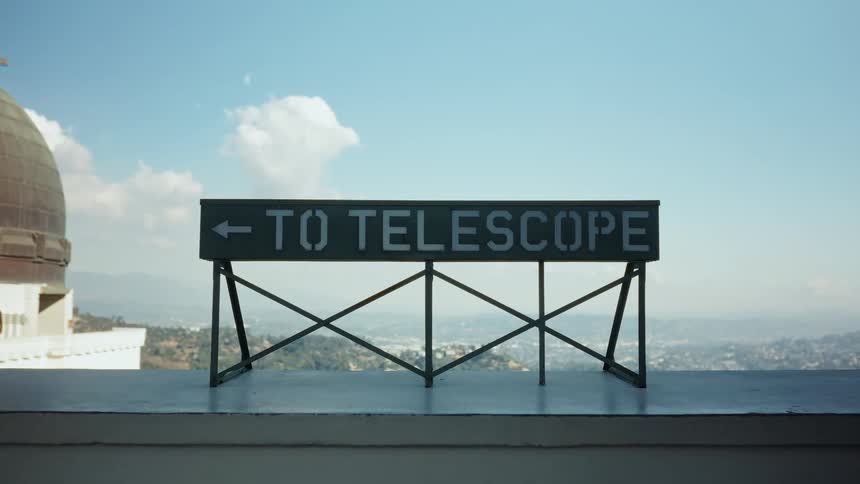 A "To Telescope" sign points the way at the Griffith Observatory, with the hazy Los Angeles cityscape in the background