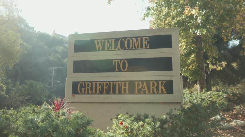 Sunlight filters through the trees to illuminate the iconic 'Welcome to Griffith Park' entrance sign
