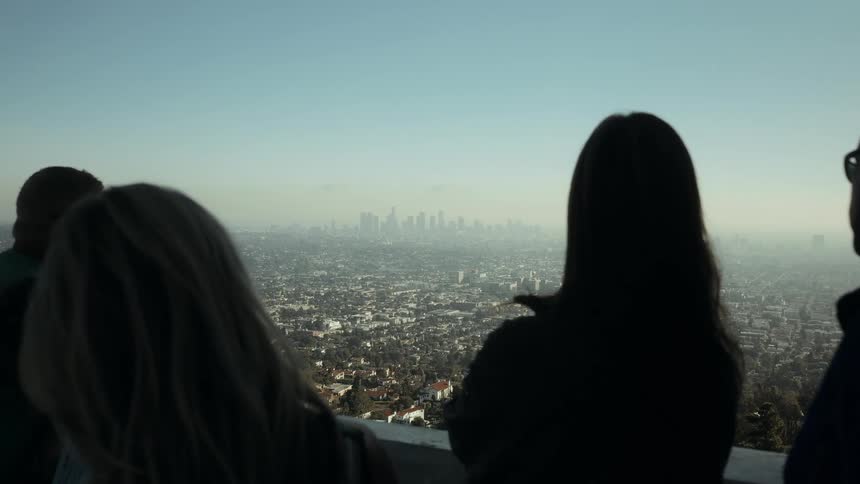 A group of friends enjoys the expansive, hazy view of the Los Angeles skyline from a scenic overlook
