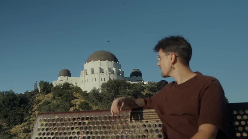 A thoughtful young man sits on a park bench and enjoys the sunny view of the Griffith Observatory in Los Angeles