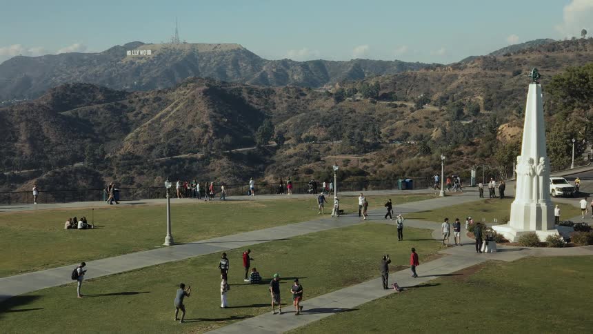 Tourists enjoy a sunny day at Griffith Observatory, taking photos with the iconic Hollywood Sign in the background