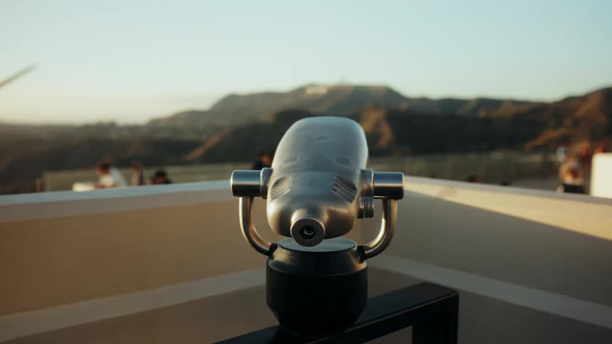 A close-up of a scenic viewpoint binocular overlooks the Hollywood Hills and the iconic sign during a warm golden hour