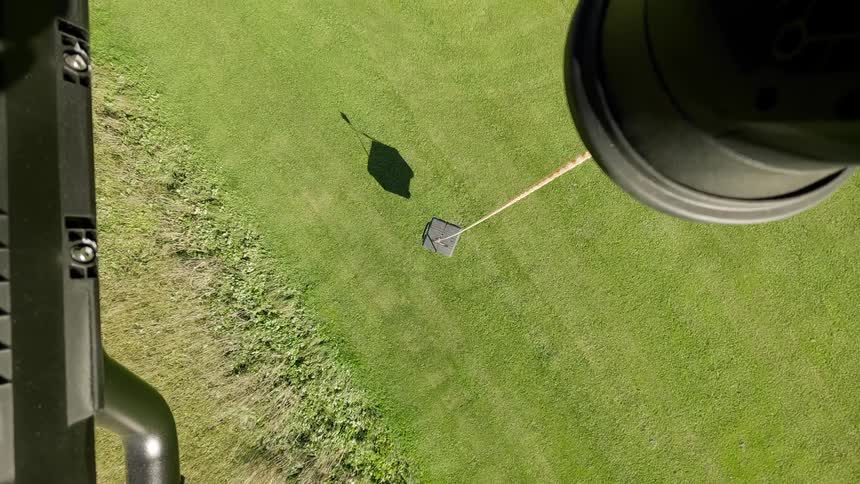 A top-down view of an automated robotic lawnmower cutting grass in a spiral pattern in a green yard