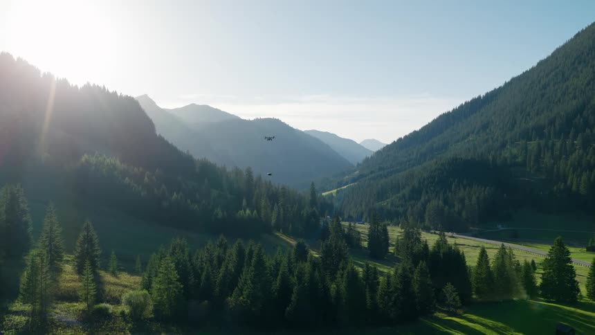 A modern delivery drone drops a package while flying over a stunning alpine valley at sunrise