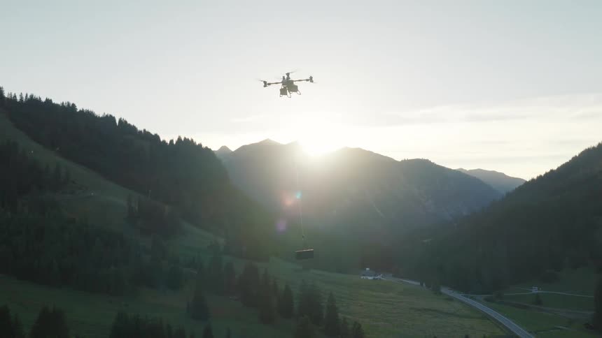 A heavy-lift delivery drone carries a payload across a scenic mountain valley as the sun rises over the peaks
