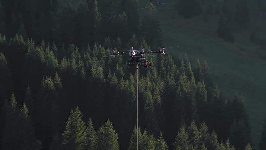 A large transport drone hovers with a long rope attached, preparing to lift cargo over a dense mountain forest