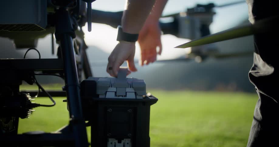 Slow motion close-up of a person removing a large battery from a drone's charging station in a backlit grassy field