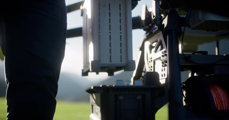 A person in slow motion removes a heavy-duty battery pack from a large agricultural drone in a sunlit field