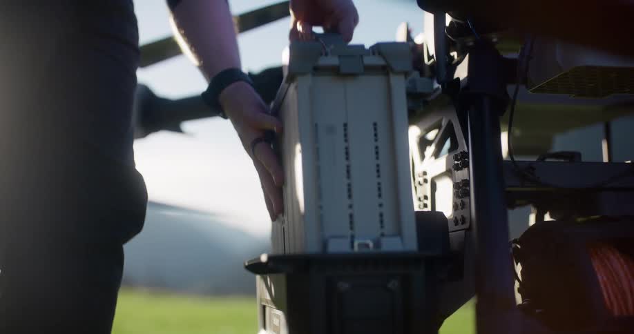 A drone technician installs a battery pack into a large professional drone in a field at sunrise