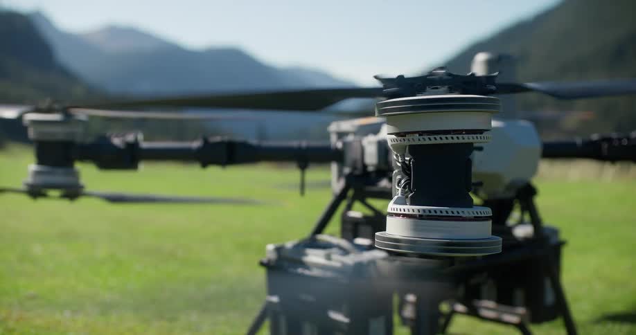 A close-up view shows the propellers of a large drone starting up and spinning in a green field