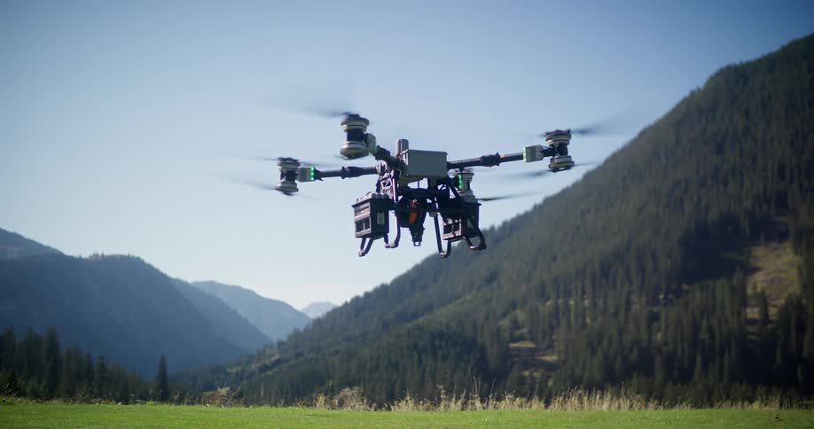 A professional hexacopter drone takes off in slow motion from a green field with a beautiful mountain landscape in the background
