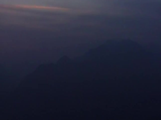 The silhouette of a mysterious mountain range looms in the dark, foggy twilight