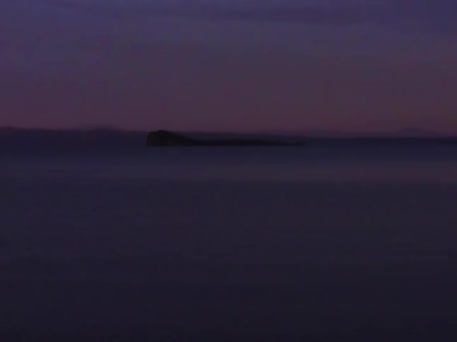A serene and moody long exposure shot of a distant island on calm water at twilight