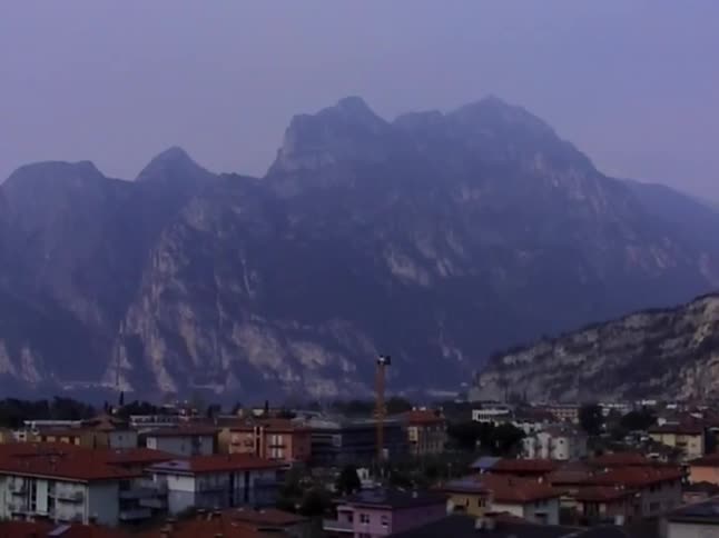 A small town with colorful buildings sits at the base of a large, hazy mountain range on an overcast day