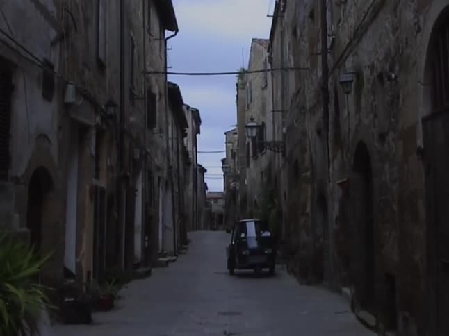 A vintage three-wheeled vehicle sits parked on a narrow street in an ancient, quiet European town