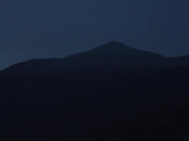 A moody slow zoom into a dark mountain peak against the deep blue twilight sky