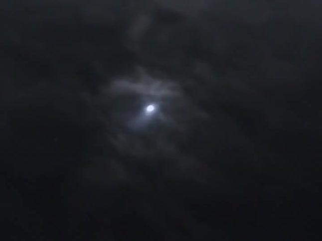 A bright moon is partially obscured by dark, wispy clouds moving across the night sky