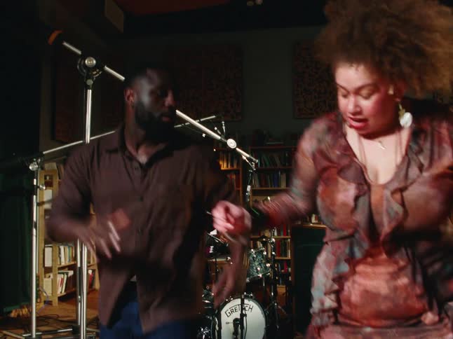 A man and woman dance with energetic abandon to the rhythm of a live jazz band in a cozy, book-lined music venue