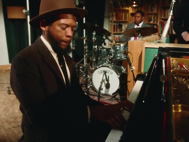 A stylish pianist in a hat soulfully plays a grand piano during a live performance with his jazz band in a dimly lit studio