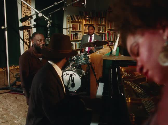 A stylish jazz quintet plays a soulful tune in an intimate, book-lined studio during a rehearsal