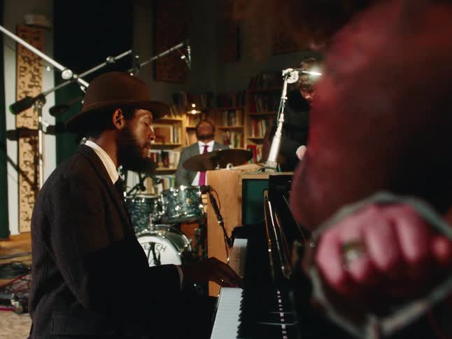 A focused pianist wearing a hat leads his jazz quartet during a soulful performance in an intimate, dimly lit studio