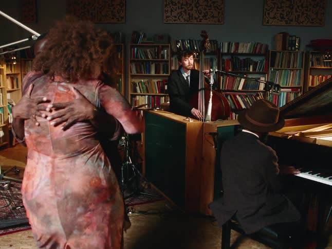 An African American couple slow dances to the sound of a live jazz trio in a cozy, book-lined room