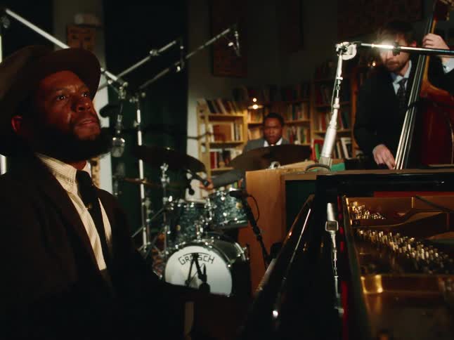 A stylish jazz trio performs a soulful piece in an intimate recording studio, with the focus on the passionate pianist