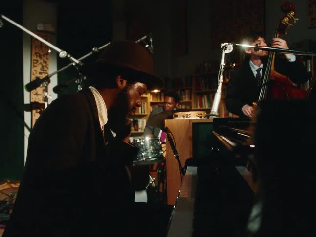 A soulful pianist plays piano and harmonica with his jazz trio in a dimly lit, intimate recording studio