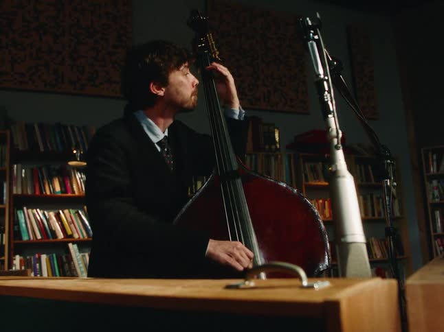 A drummer and bass player perform a jazz set together in a cozy, book-lined recording studio