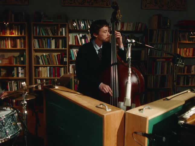 A dynamic couple dances in front of a live jazz band performing in a library before the camera slowly pushes in on the bass player
