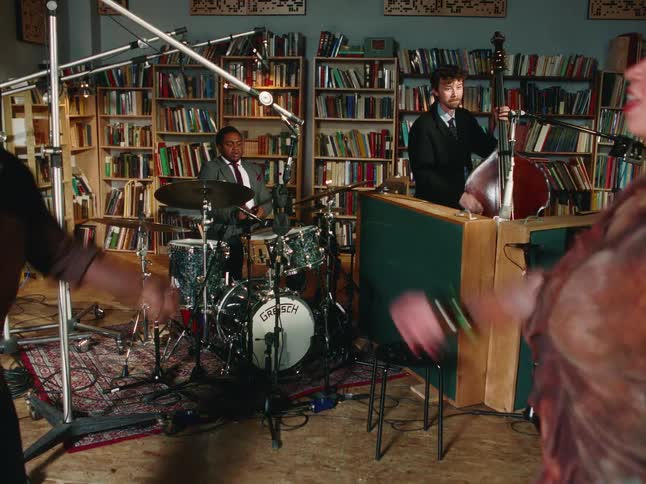 An enthusiastic couple swing dances in slow motion to a live jazz band playing in a cozy, book-lined studio
