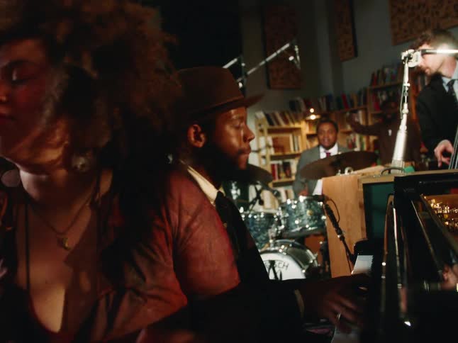 A passionate female singer with an afro grooves to the music as a pianist plays soulfully with their jazz band in a vintage studio