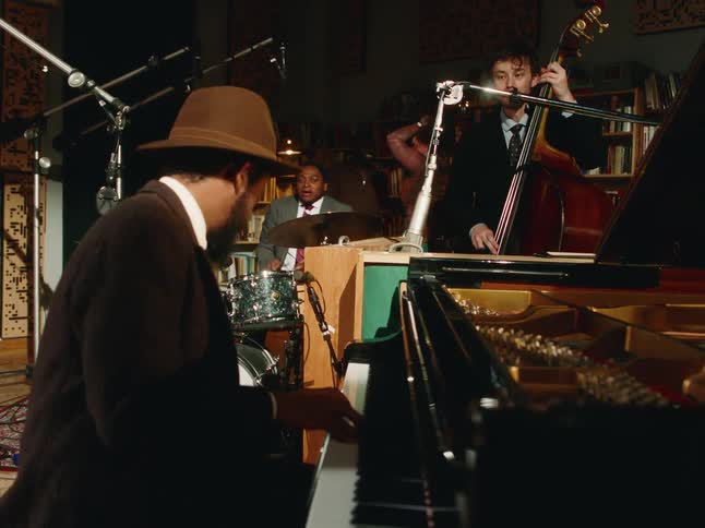 A stylish jazz trio with a pianist, upright bassist, and drummer performs an intimate set in a cozy recording studio