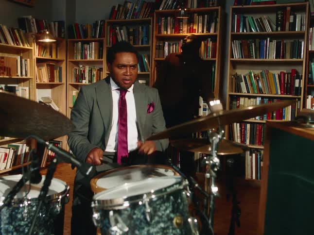 An expressive jazz drummer in a suit lays down a powerful beat while his band plays in a library-style studio
