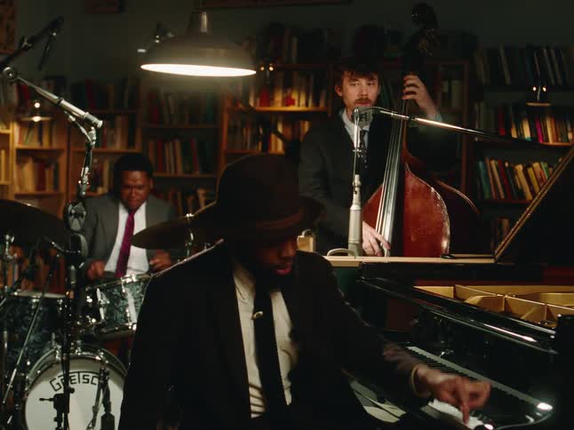 A cool jazz trio with a pianist, bassist, and drummer performs an intimate set in a vintage studio