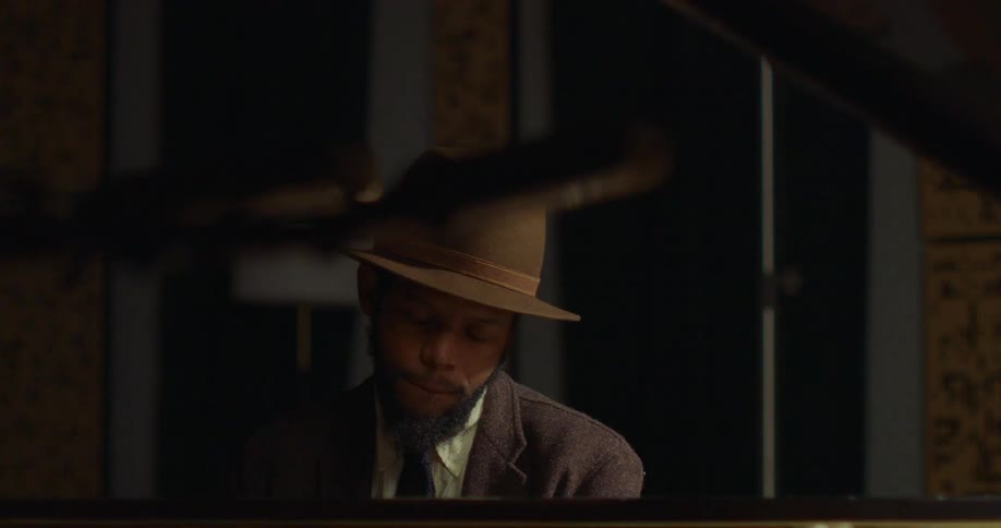 A soulful musician in a fedora immerses himself in playing a grand piano in a softly lit, intimate setting