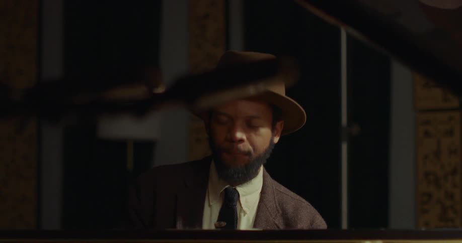 A dapper musician in a vintage hat smiles while passionately playing a soulful tune on the piano