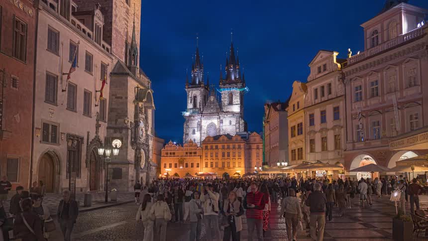 A dynamic hyper-lapse journey through the bustling crowds of Prague's Old Town Square at night, revealing the beautifully illuminated Church of Our Lady before Týn
