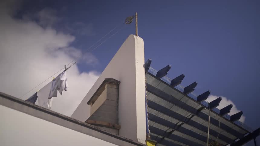 White laundry hangs from a rooftop clothesline, blowing in the wind against a bright blue sky with clouds