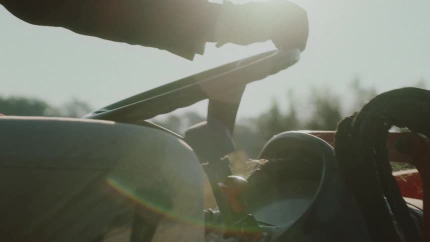 Backlit close-up of a farmer's gloved hands driving a tractor with a bright sun flare in the background