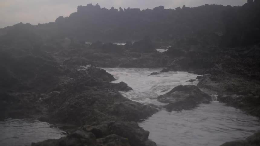Slow motion shot of ocean water flowing through misty tide pools on a rugged volcanic rock coastline