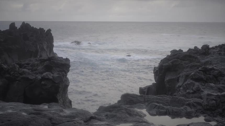 An atmospheric view of the ocean seen between two large rock formations on an overcast, gloomy day