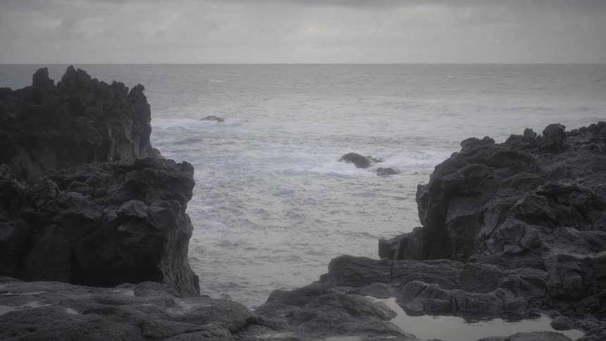 Dark volcanic rocks frame a view of the restless ocean under a gray, overcast sky