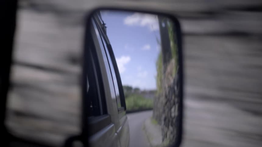 A scenic journey unfolds in the reflection of a car's side-view mirror, capturing the transition from town streets to winding country roads