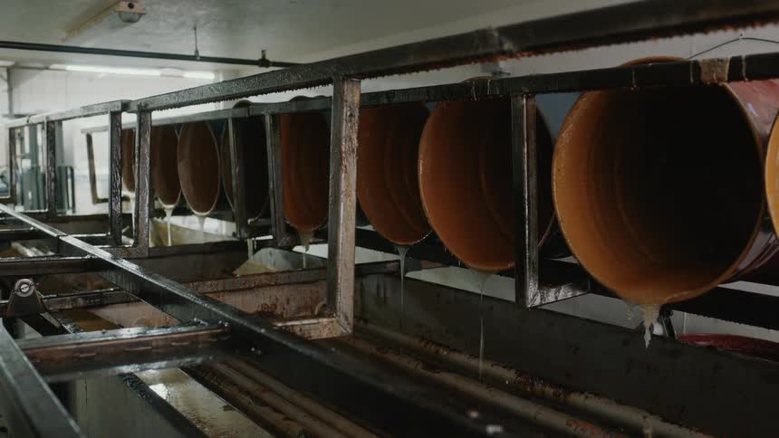 Industrial vats slowly drip thick, brown viscous liquid on a factory production line