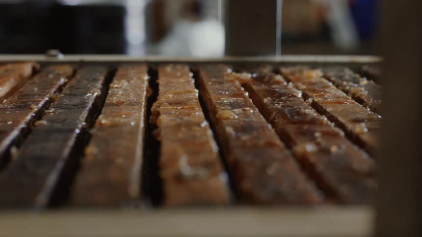 A slow, close-up pan reveals rows of wooden beehive frames coated in fresh, sticky honey
