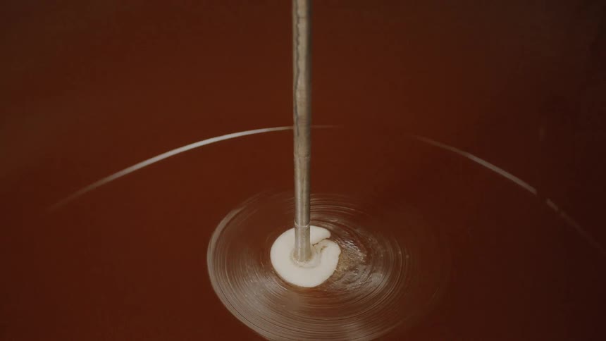 Mesmerizing top-down view of a dark brown liquid swirling into a whirlpool in an industrial brewing tank