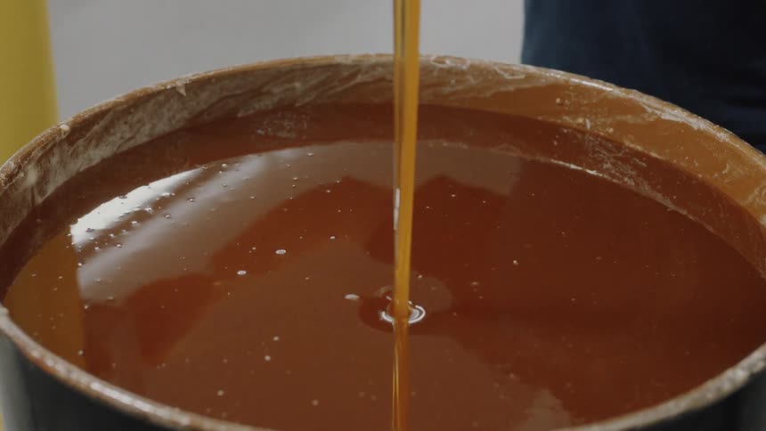 A close-up shot of thick, golden honey being steadily poured into a large barrel in a factory